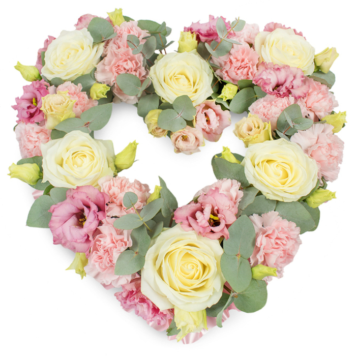 A full, symmetrical heart-shaped floral tribute is captured on a bright white background, its form lovingly built from layers of pastel blooms and soft greenery. Large cream and pale yellow roses are placed throughout the design as focal points, their velvety petals tightly coiled at the centre and expanding outwards, suggesting devotion and a carefully tended life. Interwoven with the roses are generous clusters of light pink carnations, each floret ruffled and frilly, creating a soft, almost cloud-like texture that fills the heart without a single gap. Deep pink and mauve lisianthus, also known as eustoma, are sprinkled through the arrangement, their looser, more open petals and subtle darker centres adding dimension, gentle contrast, and visual rhythm, like ripples of colour moving across the wreath. Silvery-green eucalyptus leaves curve naturally around and between the flowers, their rounded, slightly matte surfaces catching the light in cool, calming tones that frame the heart and give it structure. Small, tightly closed yellow-green buds appear in pockets around the design, introducing hints of new growth and quiet hope. The result is a dense, luxurious wreath that feels both tender and dignified, reminiscent of the peaceful atmosphere along the riverbanks in Marlow or the stillness of a churchyard in the late afternoon. This heart-shaped arrangement would serve beautifully as a funeral tribute, memorial wreath, or sympathy piece in Marlow, a visual expression of remembrance, gratitude, and enduring affection that offers gentle comfort to family and friends gathering to say goodbye.